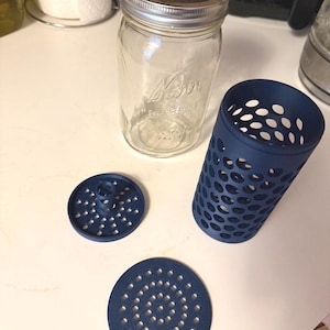 May include: A clear glass Mason jar with a silver lid, alongside three navy blue kitchen accessories. The accessories include a perforated cylinder and two circular pieces with small holes, likely for straining or draining.