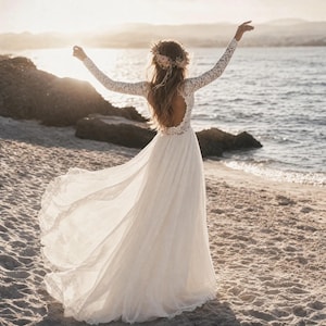 May include: A floor-length white dress with long lace sleeves, a lace bodice, and an open back. The skirt is made of a flowing, sheer fabric with a lace-trimmed hem. A floral crown is worn on the head, and the arms are raised towards the sky.