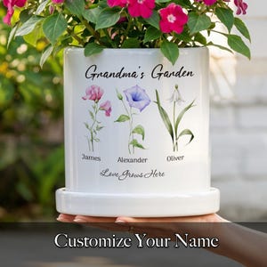 May include: White ceramic flower pot with the text "Grandma's Garden" and floral illustrations. The pot has the names "James", "Alexander", and "Oliver" below the flowers. The phrase "Love Grows Here" is also printed on the pot.