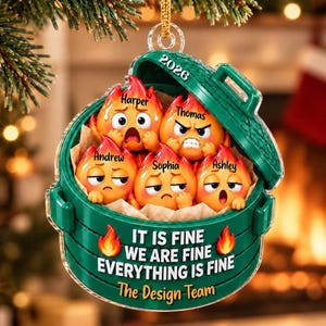 May include: A green dumpster-shaped Christmas ornament featuring five orange flame characters with various facial expressions. The names Harper, Thomas, Andrew, Sophia, and Ashley are printed above each character. The text reads 2026 and IT IS FINE WE ARE FINE EVERYTHING IS FINE The Design Team.