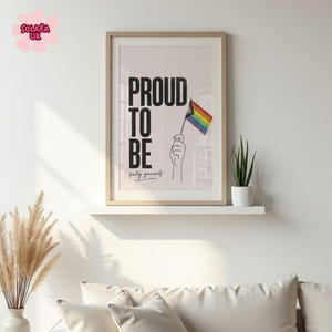 May include: A framed wall art print featuring the bold black text PROUD TO BE and the cursive text fully yourself. A line drawing of a hand holds a small rainbow flag with red, orange, yellow, green, blue, and violet stripes on a light background.