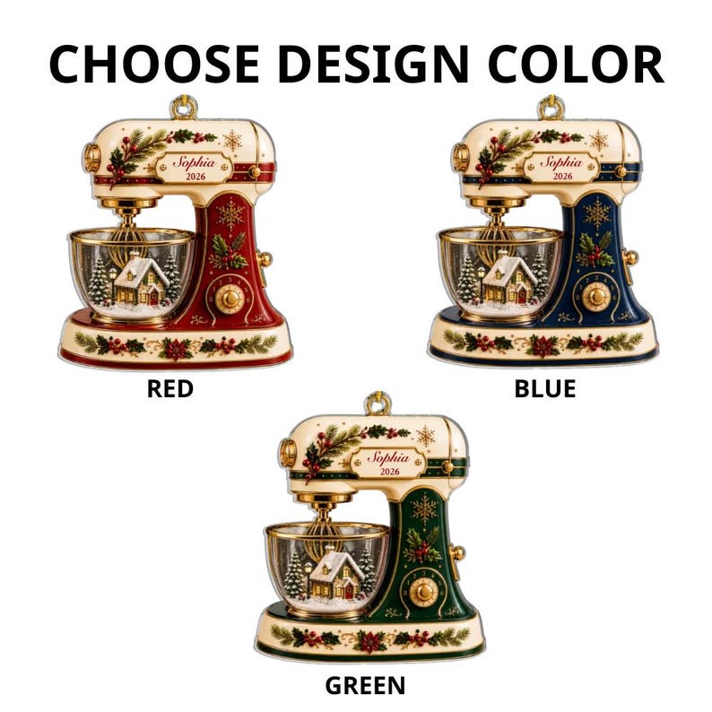 May include: Three stand mixer ornaments in red, blue, and green, each featuring a cream-colored top, gold accents, and a clear bowl containing a winter house scene. The text "Sophia 2026" is printed on the side of each mixer, with "CHOOSE DESIGN COLOR" above.