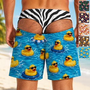 May include: Swim shorts featuring a blue water pattern with yellow rubber ducks wearing black sunglasses floating in inner tubes. The waistband has a black and white zebra stripe print. The design includes a repeating pattern of ducks.