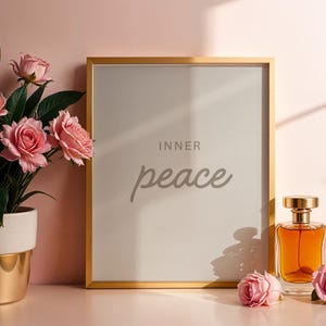 Könnte beinhalten: Ein gerahmter Druck mit den Worten "INNER peace" in einer weichen Schriftart, neben einer Parfümflasche und rosa Rosen. Der Rahmen ist goldfarben und die Parfümflasche ist mit bernsteinfarbener Flüssigkeit gefüllt. Eine Topfpflanze mit rosa Rosen befindet sich links.