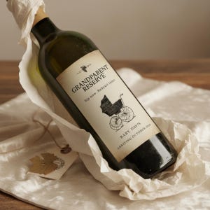 May include: A dark green wine bottle with a custom label that reads "Grandparent Reserve" and "Baby Davis Arriving October 2026". The label features a vintage baby carriage illustration. The bottle is wrapped in white paper and sits on a cream-colored surface.