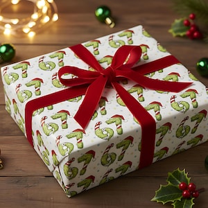 Op de afbeelding: Een ingepakt cadeau met een rood fluwelen lint. Het cadeaupapier heeft een witte achtergrond met een herhaald patroon van groene, cartoonachtige figuren met kerstmutsen. Kerstballen en hulst omringen het cadeau.