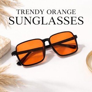 Puede incluir: Gafas de sol con montura negra y lentes naranjas. La imagen muestra el texto "TRENDY ORANGE SUNGLASSES". Las gafas tienen forma cuadrada y est&aacute;n sobre un fondo blanco. Las lentes son de color naranja brillante.
