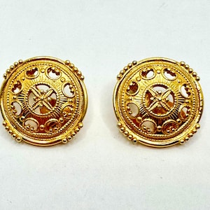 May include: A pair of gold-toned earrings with a circular design featuring intricate cutouts. The earrings have a textured surface and a raised center.