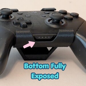 May include: Black video game controller with buttons, joysticks, and a directional pad. The controller has a built-in stand and a series of small indicator lights. The text "Bottom Fully Exposed" is visible.