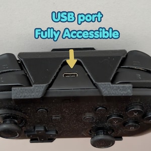 May include: Close-up of a black game controller with the text "USB port Fully Accessible" in blue and a yellow arrow pointing to the USB port. The controller has various buttons and joysticks.