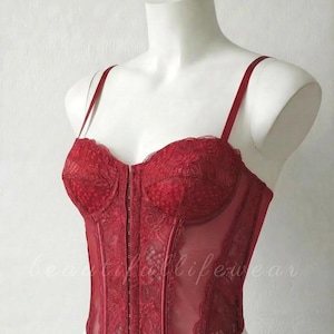 Corset bustiê estruturado em renda vermelha, top justo transparente com detalhes em botões metálicos.