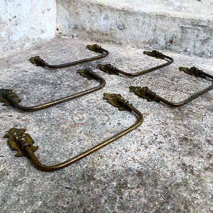 May include: Five antique brass towel bars with ornate scrollwork details. The bars are arranged in a staggered pattern on a concrete surface.