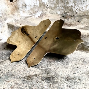 May include: Two ornate brass plates with a decorative, scalloped edge. The plates have a smooth, polished surface and a circular cutout in the centre.