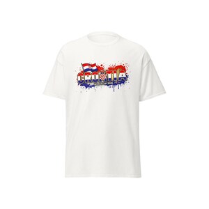 Pu&ograve; includere: T-shirt bianca con la scritta "CROATIA" in un design colorato e stilizzato, con la bandiera croata e la scritta "WORLD CUP 2026". Il design include effetti di schizzi di vernice rossa, blu e bianca.