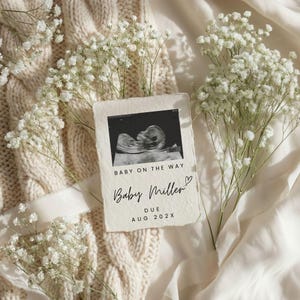 May include: A sonogram image with the text "Baby on the Way" and "Baby Miller" with a heart symbol. The due date is August 202X. The image is surrounded by white flowers and a cream-coloured knitted blanket.