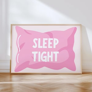 May include: A framed print featuring a pink pillow illustration with the words "SLEEP TIGHT" in white. The artwork has a light pink background and is displayed on a wooden floor.