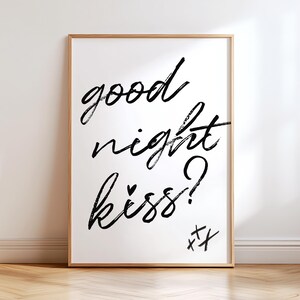 May include: A framed art print with the words "good night kiss?" in black brush lettering. The print has a white background and a wooden frame. The bottom right corner features two crossed-out X's.