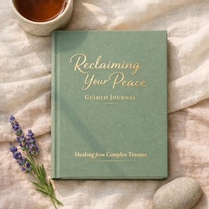May include: A sage green guided journal titled "Reclaiming Your Peace" with gold lettering, accompanied by a cup of tea, lavender sprig, and a smooth stone. The journal's subtitle reads "Healing from Complex Trauma."
