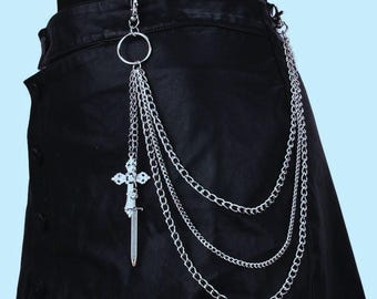 May include: Silver-colored chain belt with a decorative cross and sword pendant. The belt features multiple strands of chain and a large ring for attachment. The accessory is shown against a black garment.