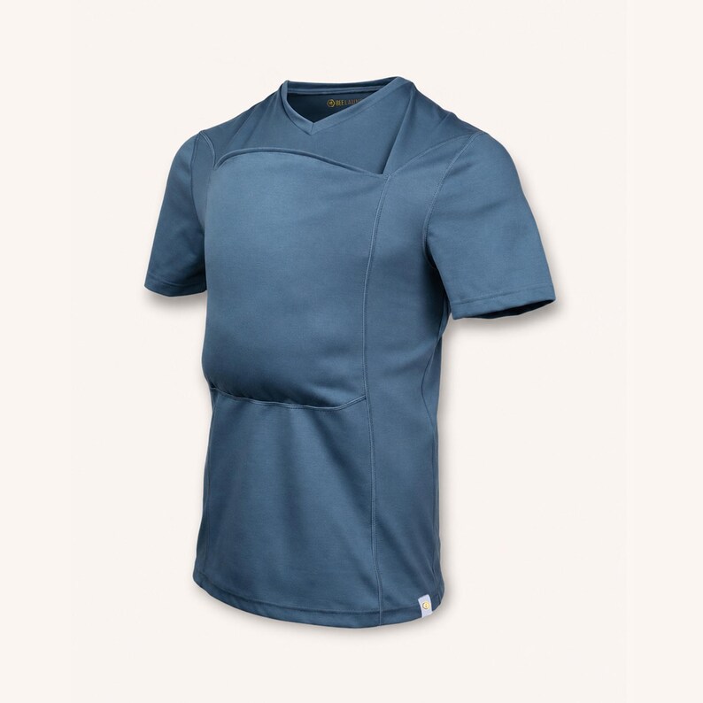 Peut inclure: Un t-shirt &agrave; manches courtes et col en V de couleur bleu ardoise uni. Le v&ecirc;tement pr&eacute;sente une construction &agrave; panneaux superpos&eacute;s distincte sur la poitrine, cr&eacute;ant un design structur&eacute;. Une petite &eacute;tiquette rectangulaire blanche est visible.