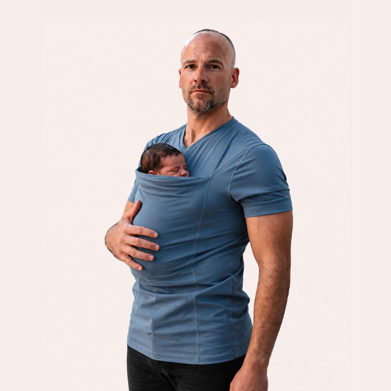 Peut inclure: Un t-shirt bleu poussi&eacute;reux &agrave; manches courtes et col en V dot&eacute; d'une poche en tissu int&eacute;gr&eacute;e sur la poitrine con&ccedil;ue pour porter un nourrisson. Le v&ecirc;tement est fabriqu&eacute; dans un tissu uni lisse et pr&eacute;sente des coutures verticales sur le devant.