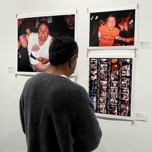 Pu&ograve; includere: Una persona guarda tre fotografie incorniciate su un muro bianco. Le fotografie raffigurano scene di concerti, tra cui una persona con una camicia bianca strappata e un'altra con una maglietta arancione con testo. Viene visualizzata anche una striscia di pellicola.
