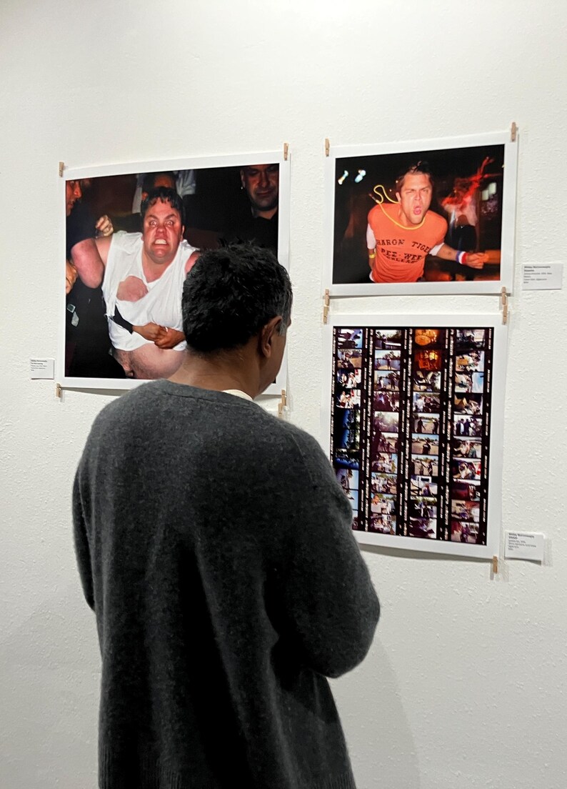 Pu&ograve; includere: Una persona guarda tre fotografie incorniciate su un muro bianco. Le fotografie raffigurano scene di concerti, tra cui una persona con una camicia bianca strappata e un'altra con una maglietta arancione con testo. Viene visualizzata anche una striscia di pellicola.