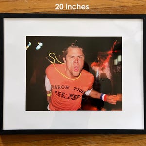 Pu&ograve; includere: Fotografia incorniciata, 51 x 41 cm, raffigurante un uomo con una maglietta arancione con la scritta "Sharon Tiger Pee Wee Kleads". L'immagine &egrave; ambientata su uno sfondo scuro con luci sfocate e l'uomo urla a bocca aperta.