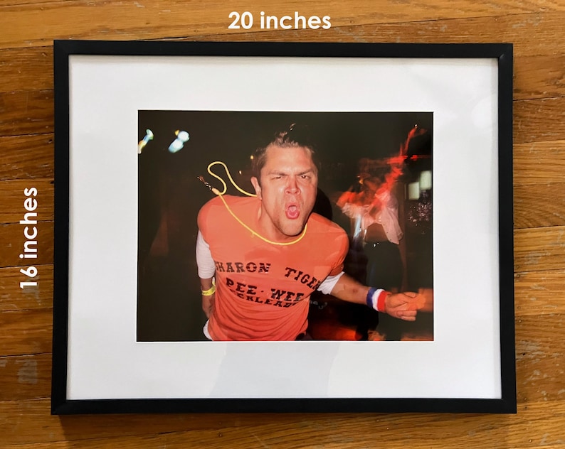 Pu&ograve; includere: Fotografia incorniciata, 51 x 41 cm, raffigurante un uomo con una maglietta arancione con la scritta "Sharon Tiger Pee Wee Kleads". L'immagine &egrave; ambientata su uno sfondo scuro con luci sfocate e l'uomo urla a bocca aperta.