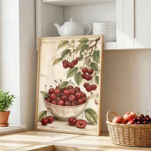 May include: A framed art print featuring a watercolor illustration of cherries. The artwork depicts a bowl overflowing with ripe red cherries, with a branch of cherries and leaves above. The print has a wooden frame and is set on a wooden surface.