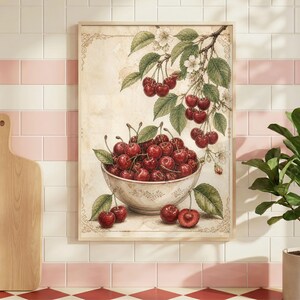 May include: A framed vintage-style print featuring a bowl overflowing with ripe red cherries. The cherries are surrounded by green leaves and a branch with white blossoms. The print has a beige background and a wooden frame.