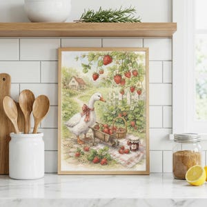 May include: A framed watercolor print depicts a goose with a red bow, a wheelbarrow, and a basket filled with strawberries. The scene includes a white picket fence, a small house, and strawberry plants. The print is in a light wooden frame.