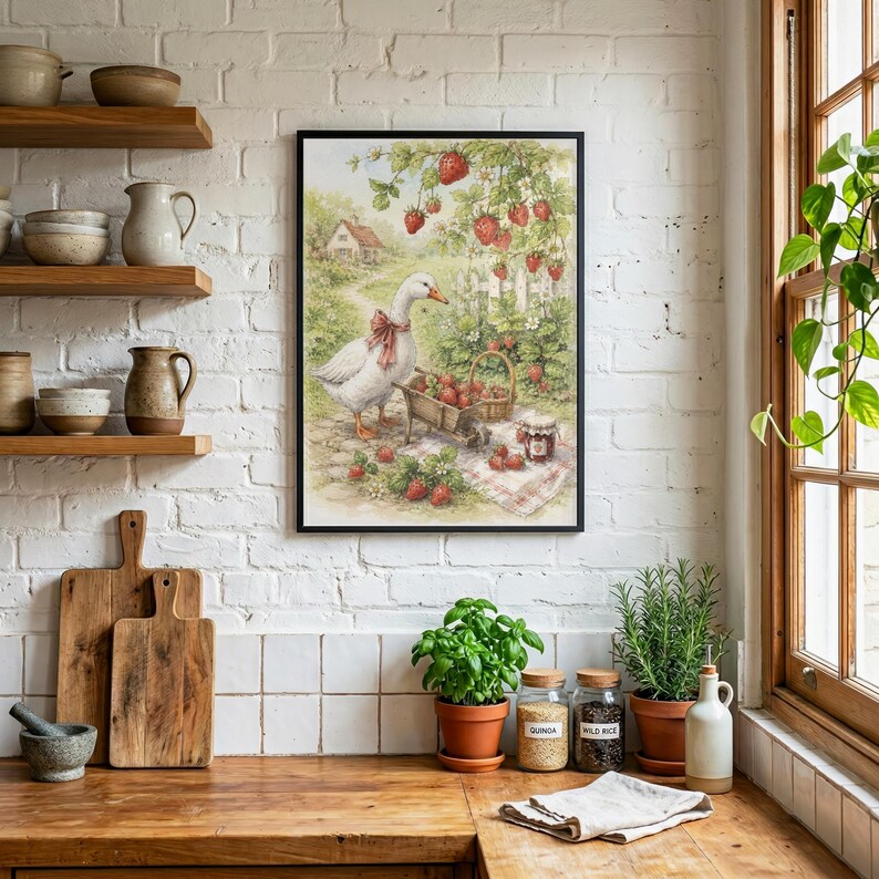 May include: A framed watercolor print depicts a goose with a red bow, a wheelbarrow, and a basket filled with strawberries. The scene includes a white picket fence, a house, and strawberry plants. The print is in a black frame.