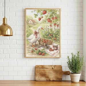 May include: A framed print of a goose wearing a red bow, standing near a wheelbarrow and basket filled with strawberries. The scene includes a white picket fence, a small house, and strawberry plants, creating a charming, pastoral aesthetic.