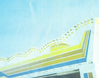 May include: A white building with a yellow and blue striped awning. The awning has a row of yellow lights along the top edge.