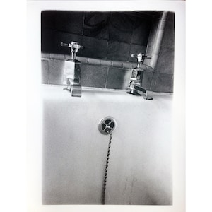 Peut inclure: Une photographie en noir et blanc d'une salle de bain vintage avec deux robinets chrom&eacute;s et un bouchon de vidange &agrave; cha&icirc;ne.