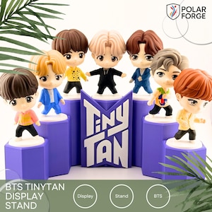 May include: A display stand with seven TinyTan figurines, each with distinct hairstyles and outfits. The figurines are on purple platforms, with a central purple display reading "TinyTan" in white. The image includes the text "BTS TinyTan Display Stand".