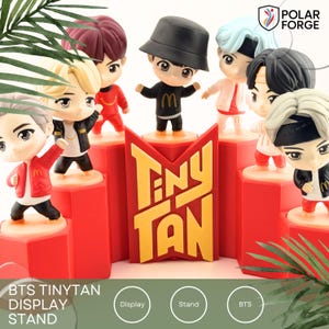 May include: A red display stand with the text "TINY TAN" and several small cartoon character figurines. The figurines are on red platforms. The stand has a "Polar Forge" logo.