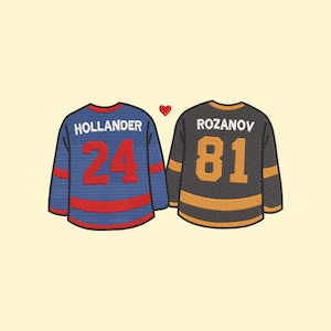 Pode incluir: Duas camisas de hóquei lado a lado com um coração vermelho entre elas. A camisa da esquerda é azul com listras vermelhas e o nome "HOLLANDER" e o número "24". A camisa da direita é preta com listras douradas e o nome "ROZANOV" e o número "81".