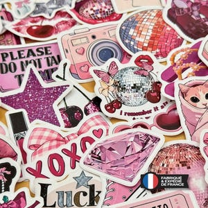 Op de afbeelding: Een verzameling diverse stickers met roze en paarse thema's, waaronder discoballen, een camera, een diamant, kersen, een kat, een ster, een strik en tekstelementen. De stickers zijn in een dichte, overlappende collage bij elkaar geplaatst.