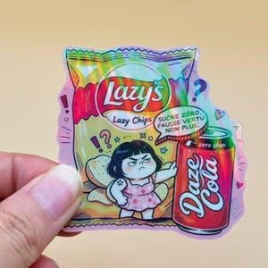 Puede incluir: Una pegatina holográfica con una bolsa de Lazy's Lazy Chips y una lata roja de Daze Cola. Un personaje de dibujos animados con pelo negro y vestido rosa de flores se sitúa entre ambos. Un bocadillo de texto dice: SUCRE ZÉRO, FAUSSE VERTU NON PLUS.