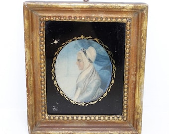 May include: A rectangular gold-toned frame with a beaded inner border surrounds a black glass panel. Centered is an oval portrait miniature of a person in profile, wearing a light-colored head covering and garment, enclosed by a thin gold filigree.