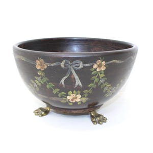Peut inclure: Un bol en bois brun foncé avec un motif floral et des pieds en forme de griffes en laiton. Le bol présente une guirlande de fleurs peintes et un ruban. L'intérieur du bol est d'une nuance de brun plus foncée.