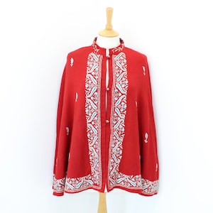 Peut inclure: Une veste rouge de style cape avec des motifs floraux brodés blancs et bleus. La veste a un col mandarin et des fermetures à boutons. La broderie présente un motif de type cachemire le long des bords et du devant.