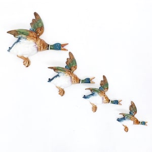 Puede incluir: Un conjunto de cuatro patos reales de cerámica para montar en la pared en tamaños descendentes, cada uno con un acabado brillante y detalles pintados que incluyen cabezas verdes, pechos blancos, cuerpos marrones y alas con puntas azules.