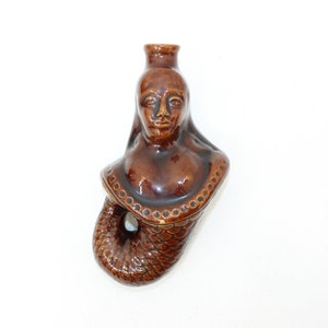Pode incluir: Uma garrafa de cerâmica marrom em forma de sereia com um rosto detalhado e uma cauda escamosa.