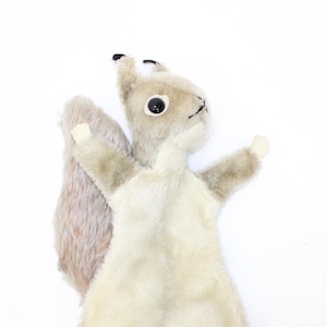 May include: A plush gray and white squirrel puppet with black eyes and a long tail. The puppet has a hand opening for a finger to fit inside to operate the puppet.