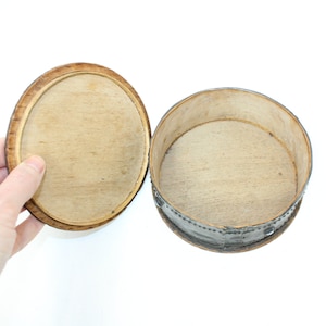 May include: A round wooden box with a lid. The box is made of light wood and has a dark brown rim. The lid is open and the inside of the box is empty.