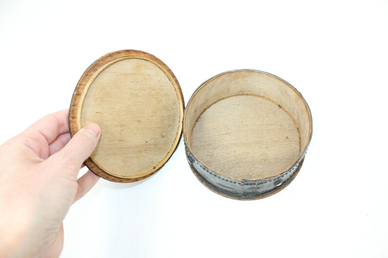 May include: A round wooden box with a lid. The box is made of light wood and has a dark brown rim. The lid is open and the inside of the box is empty.