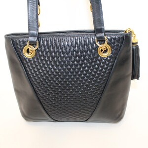 May include: Black leather tote bag with gold-tone hardware. The bag features a quilted center panel and smooth side panels. Includes a tassel zipper pull and double shoulder straps.